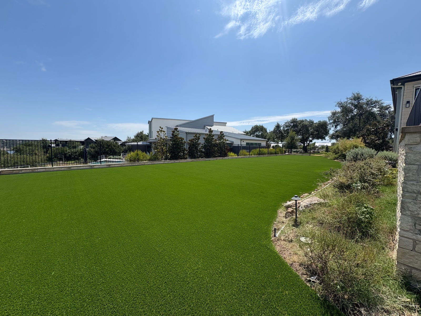 Freshly installed artificial grass lawn bordered by landscaped beds and an iron fence
