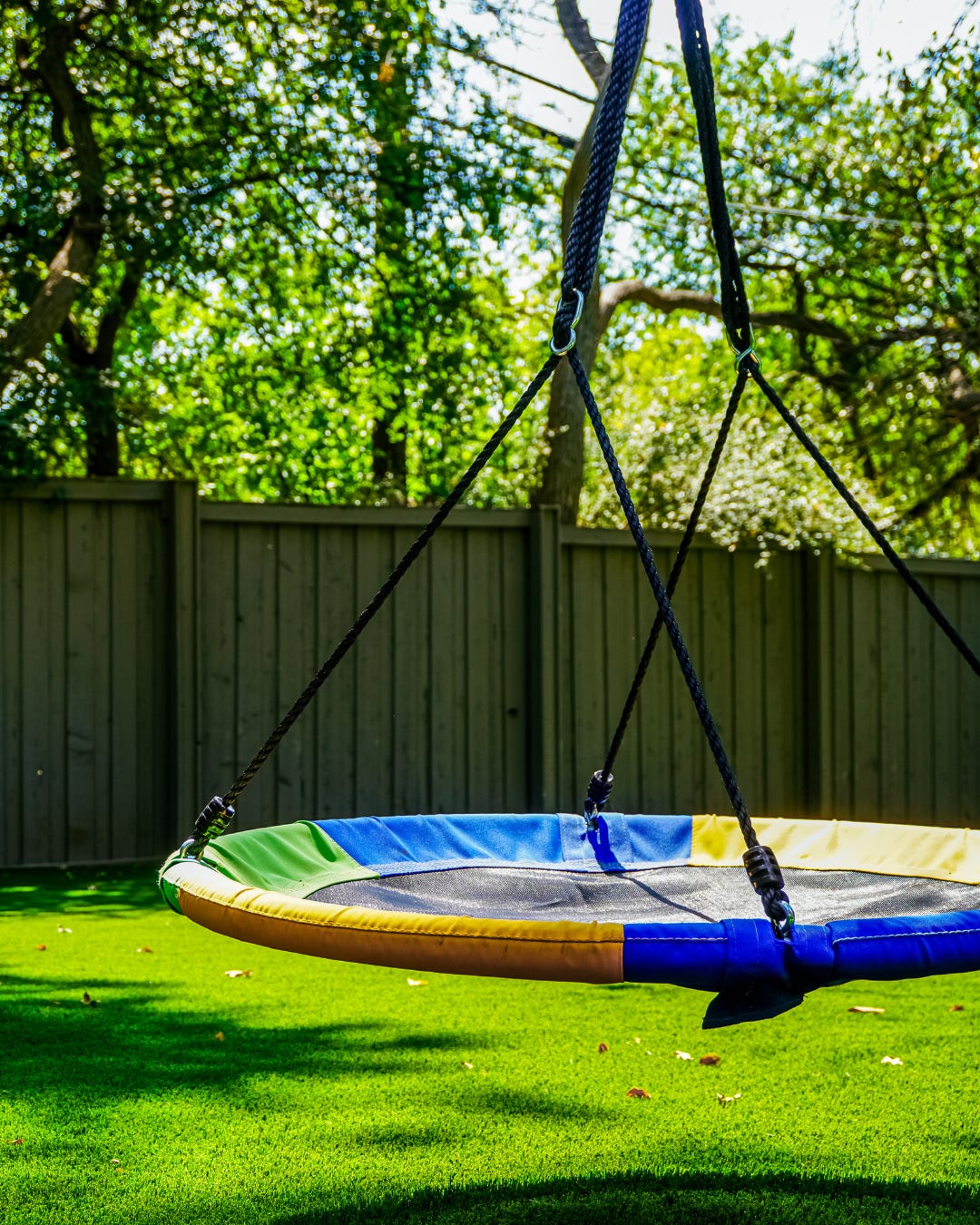 Saucer swing hanging over an artificial grass backyard lawn