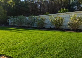 Artificial grass lawn meeting a paver edge below a stone retaining wall