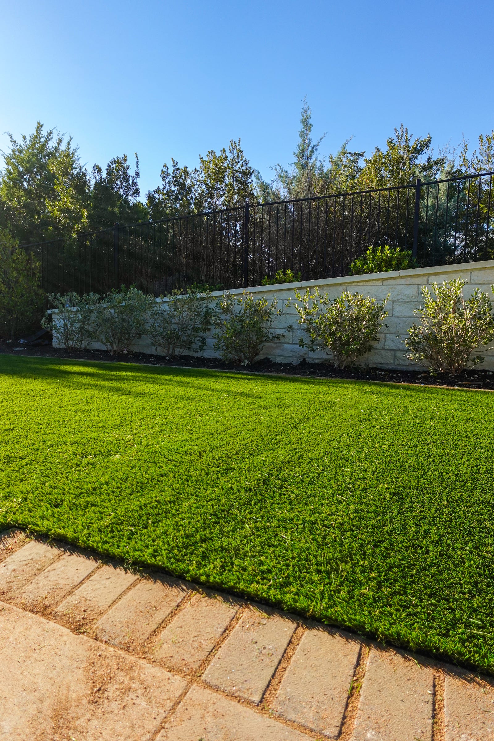 Artificial grass lawn meeting a paver edge below a stone retaining wall