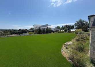 Wide artificial grass lawn installed along a landscaped bed and iron fence